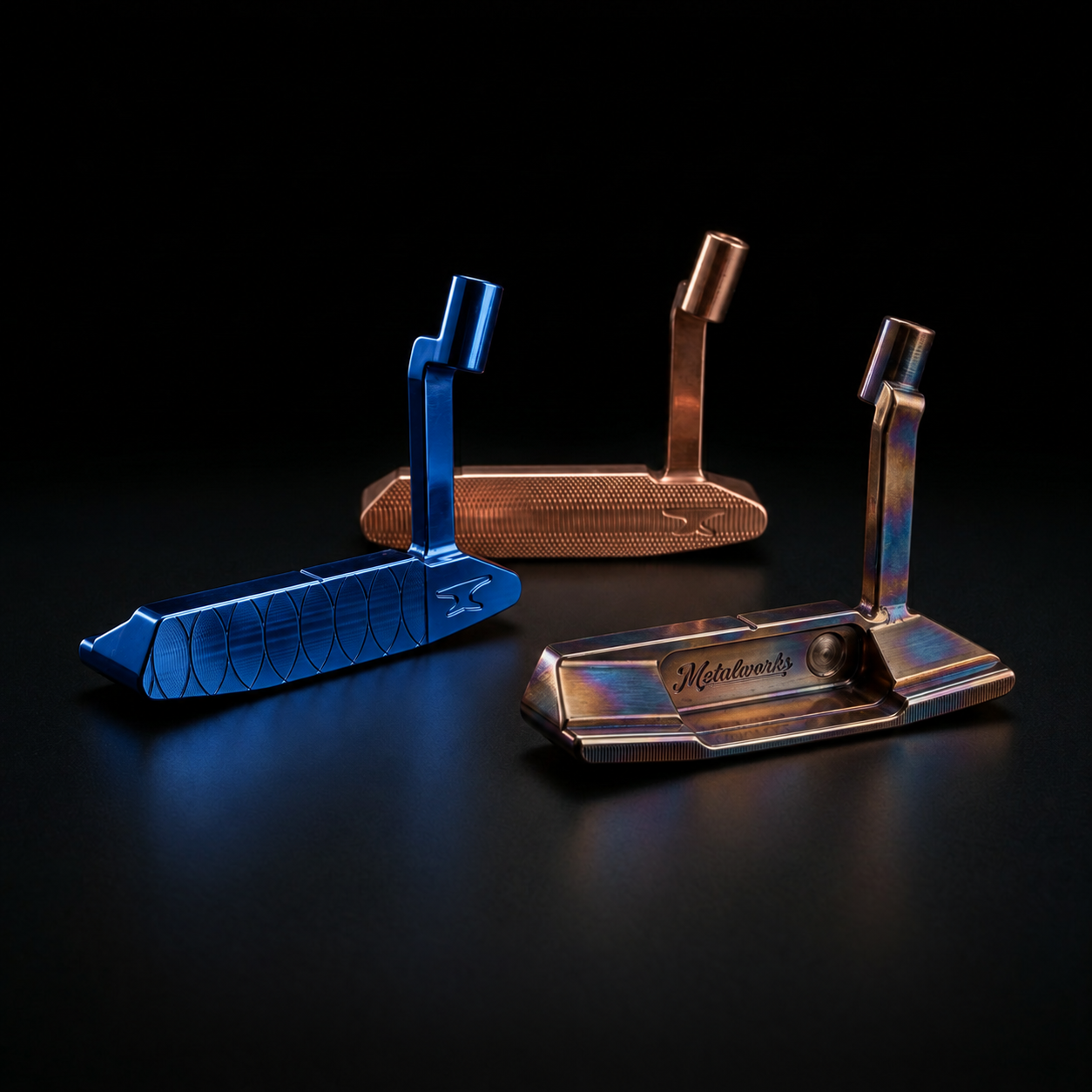 Three Metalworks custom milled blade putters under a spotlight